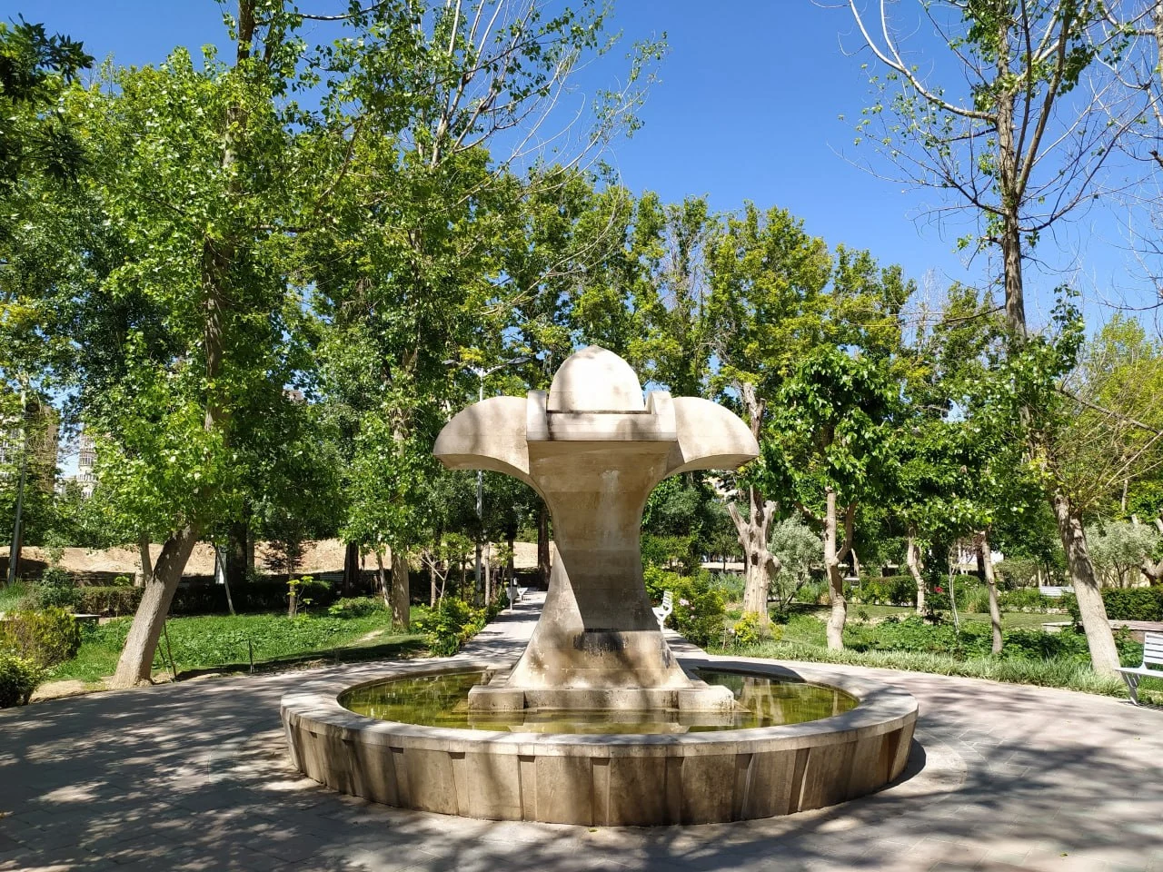 آبنمای سنگی در میان فضای سبز یکی از پارکهای تهران با درختان سرسبز و مسیر پیادهروی